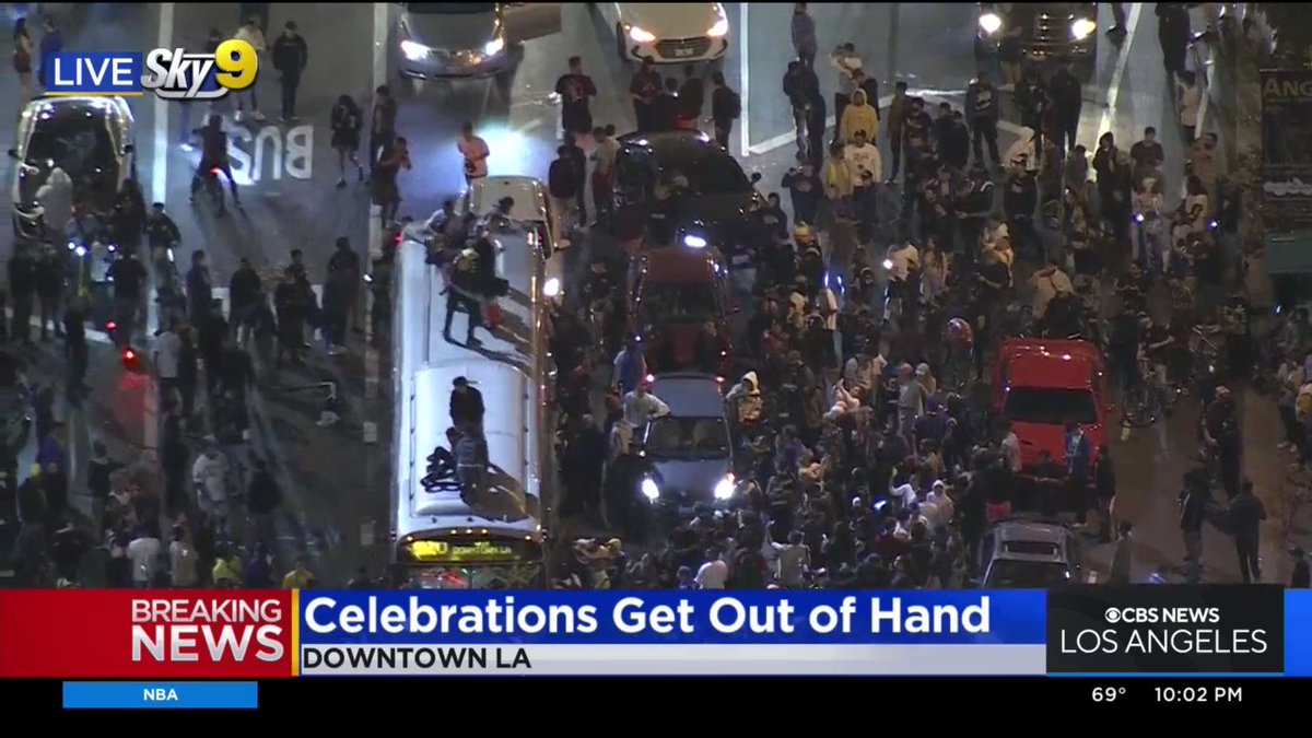 Unruly crowds can be seen jumping on top of a bus while also vandalizing the front windshield