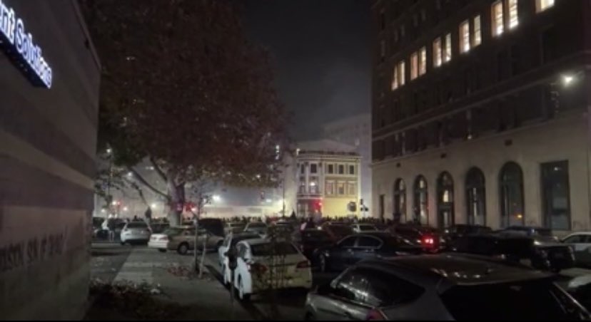 17th & San Pablo Ave. Cars skate past @OICSharksIce Center & landmark Maclise Drugstore Bldg blocks from @Oakland City Hall. @BMW set on fire. @oaklandpoliceca arrive to disperse participants